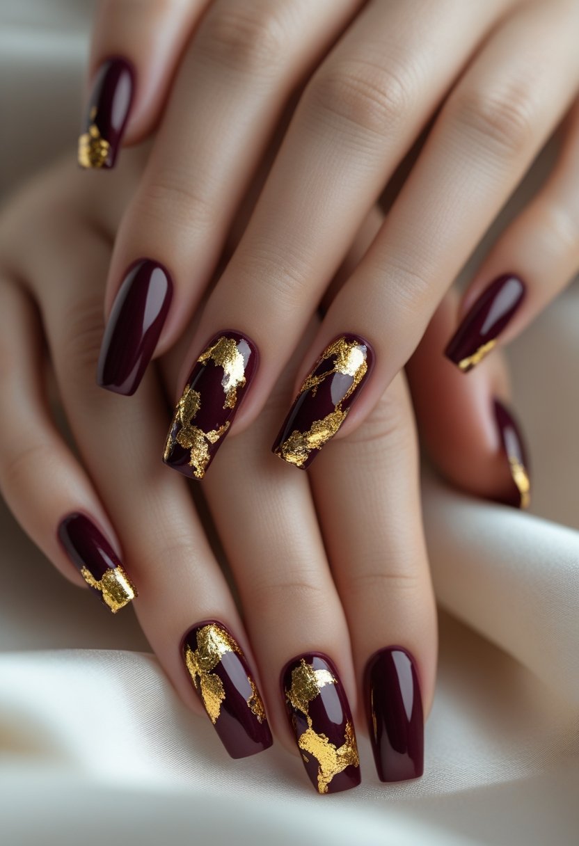 Close-up of hands with burgundy and gold foil decorated nails against a neutral background.
